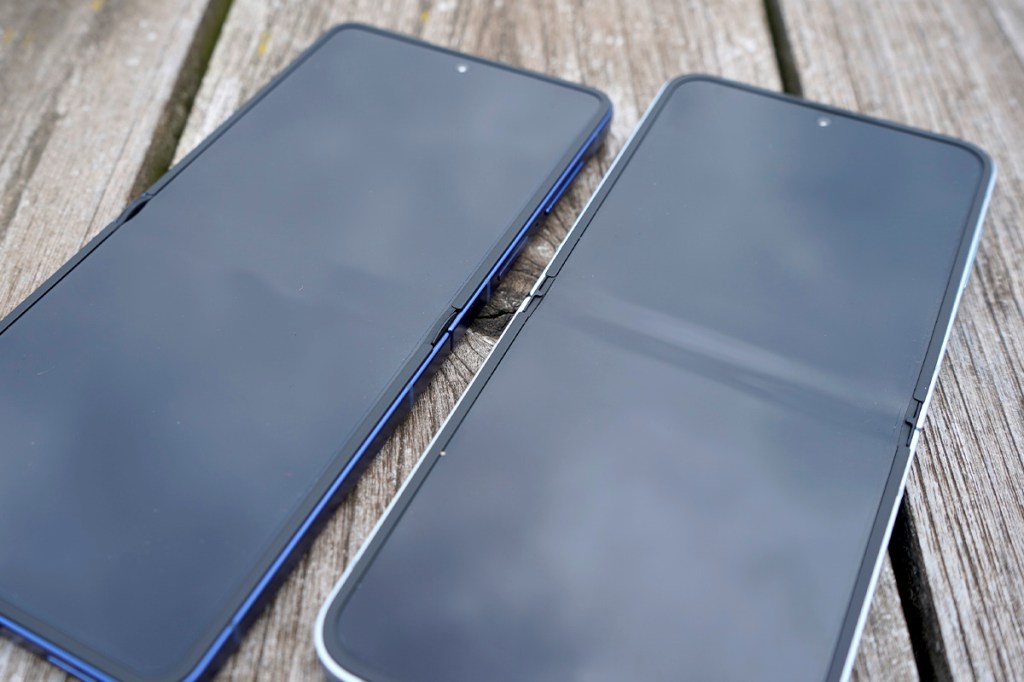 Zwei Smartphones liegen mit abgeschaltetem Display nebeneinander auf einem Holztisch.