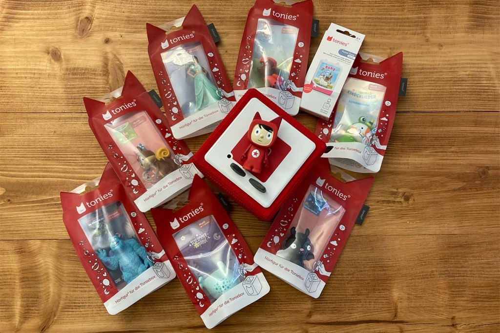 rote Toniebox mit rotem Kreativ-Tonie, auf einer Holzunterlage, rumherum viele verpackte Tonie