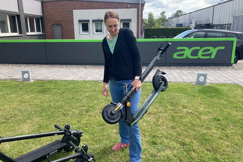Frau trägt einen zusammengefalteten E-Scooter
