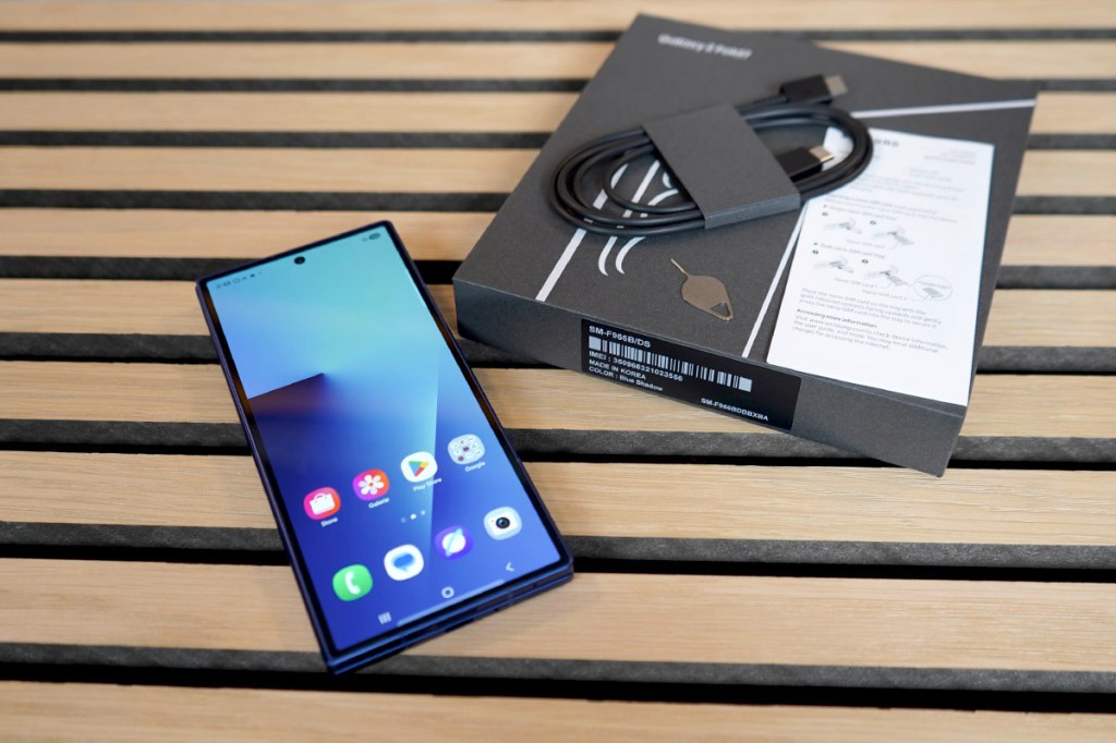 Ein Smartphone liegt neben der Verpackung und Zubehör auf einer Holzfläche.